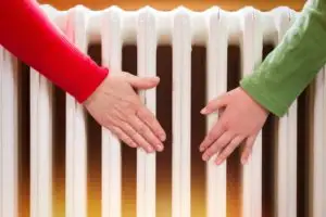 Two people warming their hands on a radiator to combat the cold.