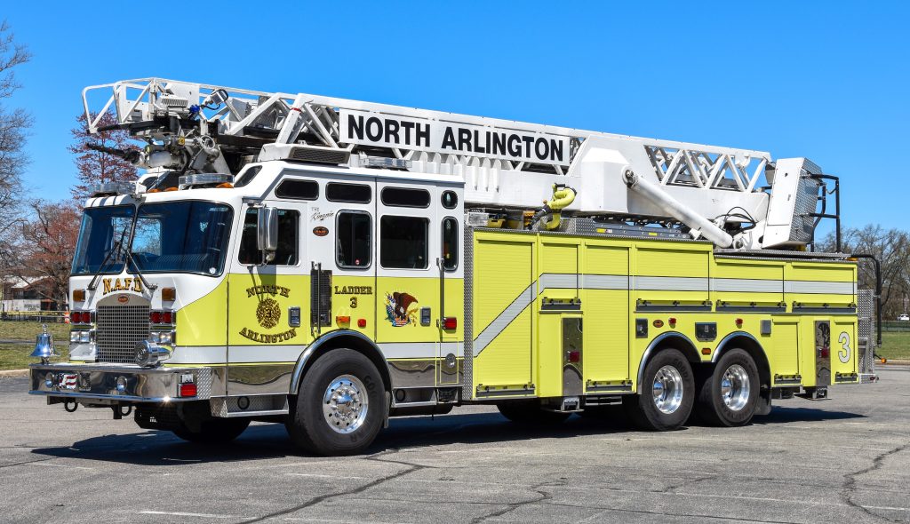 A yellow and white fire truck labeled "North Arlington" with a large extendable ladder parked in a lot on a clear day. The truck has three axles and is marked "Ladder 3" on the side.