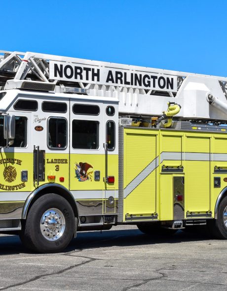 A yellow and white fire truck labeled "North Arlington" with a large extendable ladder parked in a lot on a clear day. The truck has three axles and is marked "Ladder 3" on the side.